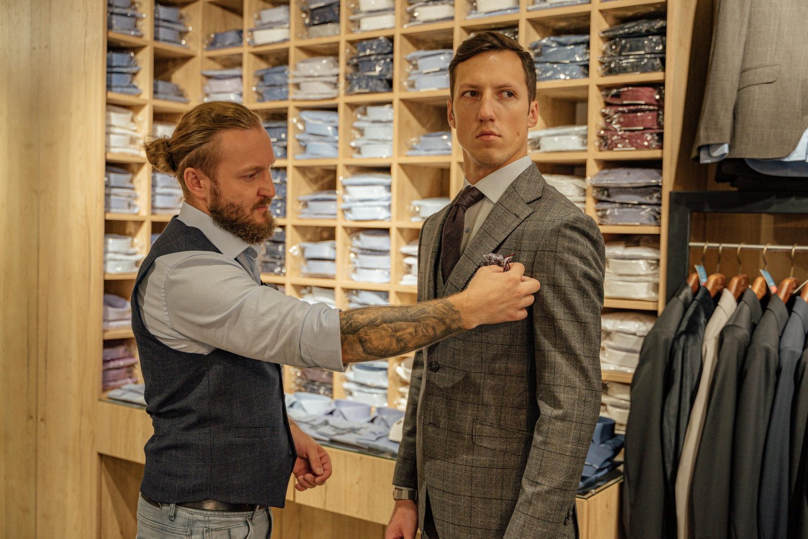A tailor assists a man with a suit jacket fitting in a clothing store.
